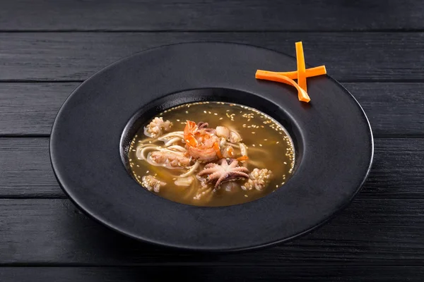 Seafood soup with squid, octopus, shrimp, eel, mussels, snails. Tom Yam soup with seafood. Spicy Asian Seafood Soup on black dish, thai cuisine.Bowl of fresh seafood soup. — Stock Image Seafood Soup Squid Octopus Shrimp Eel Mussels Snails Tom Yam Royalty Free Stock Photos