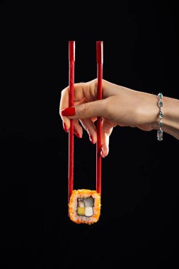 Kadın elinde yemek çubuklarıyla suşi tutuyor. Elinde yemek çubuklarıyla elinde suşi tutan genç bir kadın. Elleri çubuk tutan bir kadınla suşi sarması.