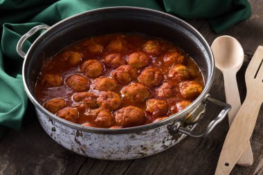 Geleneksel İtalyan köfteleri eski ahşap bir masada servis edilir. Köfteler, yeşil peçete ve kaşıkla eski ahşap bir masada servis ediliyor. Ev yapımı lezzetli İtalyan köfteleri kırsal bir masada akşam yemeği için. İtalyan mutfağı..