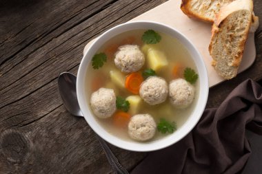 Bir kase tavuk çorbası. Köfteli, patatesli, havuçlu ve arka planda maydanozlu ev yapımı tavuk çorbası. Eski ahşap bir masada kızarmış ekmeklerle servis edilmiş. Yukarıdan bak. Üst Manzara. Yakın çekim.. 