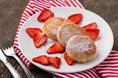 Peynirli ve çilekli krep. Çilekli ve kremalı peynirli kek. Krepler kırmızı peçeteli eski ahşap bir masada servis edilir. Kahvaltı için harika. Yakın plan çekim. Metin için boş alan.