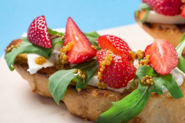 Peynirli, roka ve mavi arkaplanlı çilek. Zeytinyağına bulanmış kızarmış İtalyan ekmeği. Sabah kahvaltısı. Yakın plan çekim. Metin için boş alan.