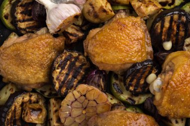 Kızarmış sebzeli tavuk butları. Tavuk eski ahşap bir masada kızartma tavasında servis edilir. Limonlu tavuk, kabak, patlıcan, soğan ve sarımsak. Yakın plan çekim. Metin için boş alan.