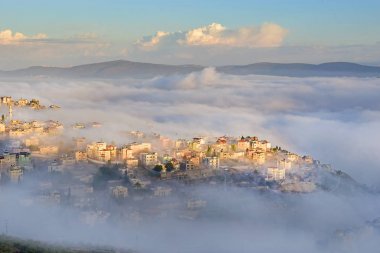 view of the shrouded in the morning fog biblical village Cana of Galilee ( Kafr Kanna ), neighborhood Nazareth in Israel, place where Jesus Christ showed first miracle clipart