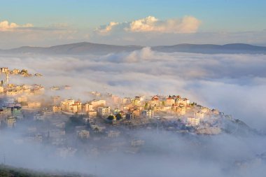 view of the shrouded in the morning fog biblical village Cana of Galilee ( Kafr Kanna ), neighborhood Nazareth in Israel, place where Jesus Christ showed first miracle clipart