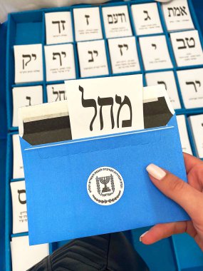 Kadın eli, üzerinde farklı İsrail siyasi partilerinin oy pusulaları olan bir zarf tutuyor. İbranice metin. İsrail Knesset Seçimleri