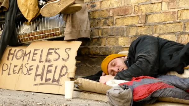 Бездомний чоловік обертається під час сну, візок з речами поруч з ним . — стокове відео