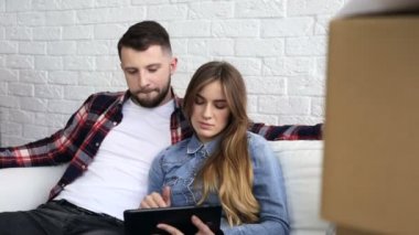 Yer değiştirme. Ciddi bir değil gülümseyen çift kanepede, kullanıcıların dijital tablet kullanarak oturan.