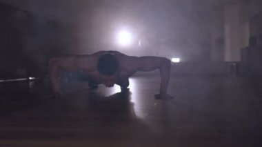 Dolly vurdu. Spor salonunda egzersiz yukarı itin yapan kaslı erkek. Arka ışık duman.