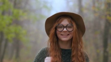 Happy and smiling young red hair woman walking in the foggy autumn park.
