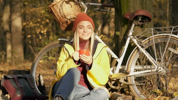 在秋天的森林里 女人坐在自行车旁边 享受着美妙的秋天 喝着热茶 或咖啡 — 图库视频影像