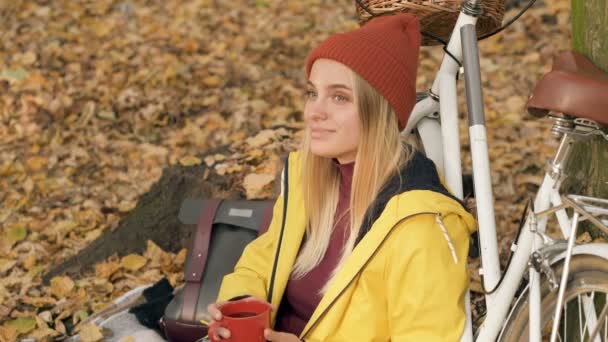 年轻女子在秋天的公园里骑自行车 喝着热咖啡 — 图库视频影像