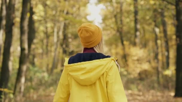 穿着黄色雨衣的女人走在秋天的森林里 从后面看 — 图库视频影像