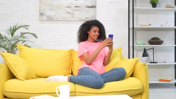 年轻女子坐在黄色沙发上 手持手机 拍了一张广角镜头 冷静的情绪 手持射击 — 图库视频影像