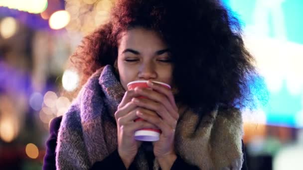 夕方の通りに熱いコーヒーを片手に立つ若いアフロアメリカ人女性の肖像画 カメラを見て微笑んだり笑ったり — ストック動画