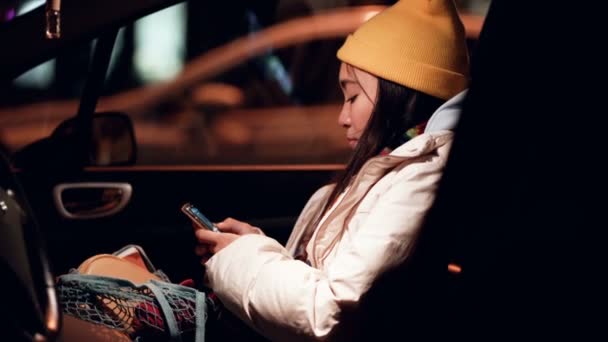 若い女性は夜の時間に車の中で座って スマートフォンを保持し 入力します 手持ち撮影 — ストック動画