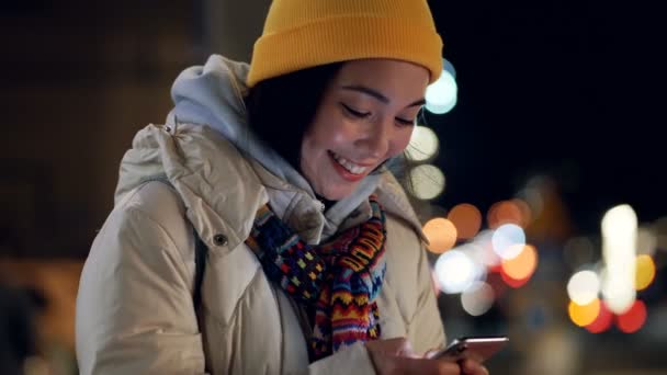 兴高采烈的亚洲女人站在街头 手里拿着智能手机和打字的信息 微笑和积极向上的情绪 Gimbal Shot — 图库视频影像