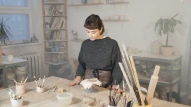 Sanat atölyesinde çalışan çömlekçi kadın. Seramik heykeli için kil hazırlıyorum. Geniş açı. El kamerasıyla..