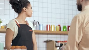 Mutlu, gülümseyen ve arkadaş canlısı Afroamerikan kadın erkek müşteriyle konuşuyor, hizmet ediyor ve sipariş alıyor. Düşük açı, el kamerası..