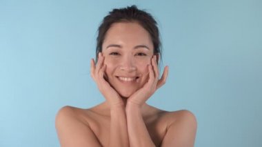 Yanaklarına krem sürmüş Asyalı genç bir kadının portresi. Sevimli ve güzel duygular. Mavi arkaplan.