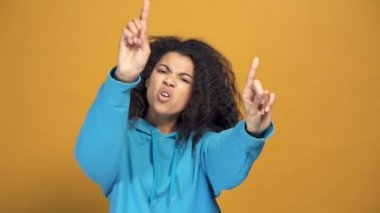 Biraz vahşi görünümlü Afro-Amerikalı bir kadının portresi dans ediyor ve şarkı söylüyor, sarı arka plan. Yavaş çekim.