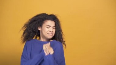 Genç afro-amerikalı kadın seviniyor ve dans ediyor. Sarı arka plan. Yavaş çekim.