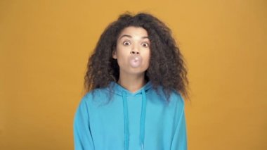 Afro-Amerikan kadın portresi. Sakız gösteriyor ve üflüyor. Yavaş çekimde. Sarı arkaplan.