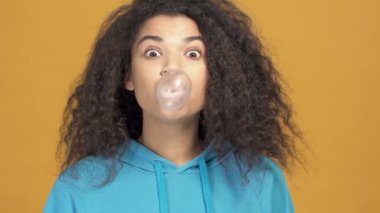 Afro-Amerikan bir kadının sakız şişirme portresi. Yavaş çekimde. Sarı arkaplan.