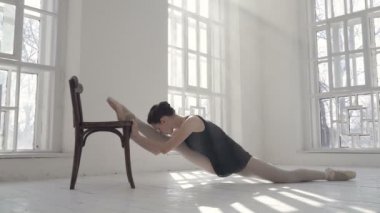 Balerin sandalyede iki büklüm oluyor. İçeride, bale stüdyosunda. El kamerasıyla..