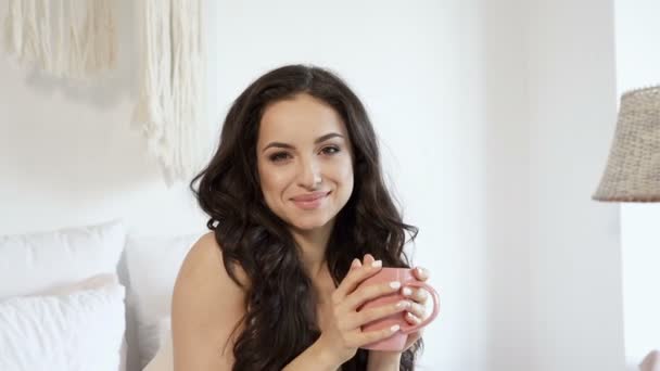 一个快乐微笑的黑发女人躺在床上喝咖啡的画像 — 图库视频影像