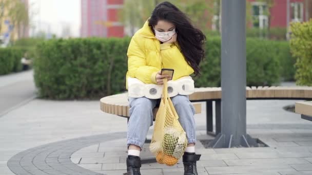 Sorglig Kvinna Bär Skyddsmask Sitter Bänken Och Tittar Smartphone Handhållen — Stockvideo