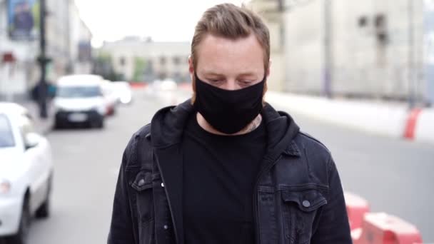 黒い顔のマスクをした男が通りを歩いて肘でくしゃみをする スローモーション — ストック動画