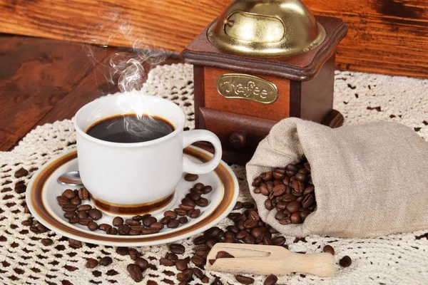 Granos de café recién molido en una bolsa junto a una taza de bl caliente — Foto de Stock