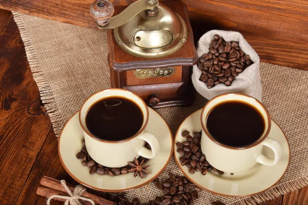 Ziarna kawy w szary worek obok młynek do kawy i dwa Puchary — Zdjęcie stockowe
