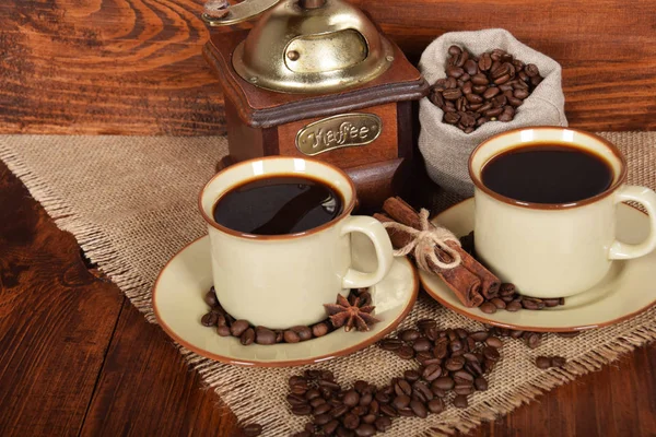 Grains de café dans un sac gris à côté d'un moulin à café et deux tasses — Photo