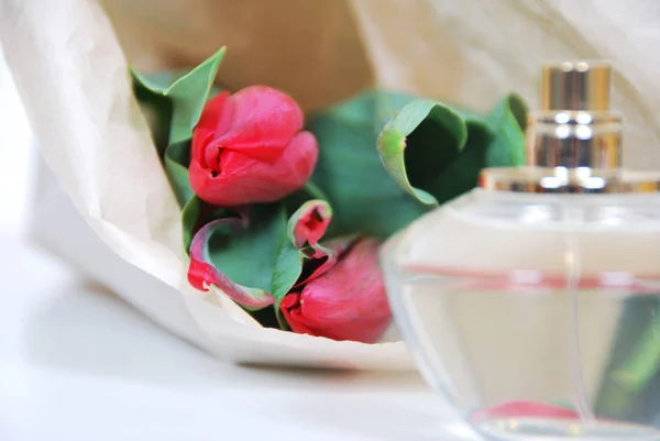 Profumi di fiori in una bottiglia di vetro e tulipani rossi — Foto Stock