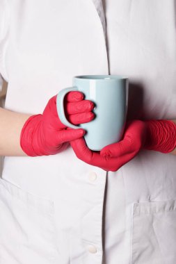 Bulaşıcı bir savaşta kırmızı eldivenli bir hemşire tarafından tutulan mavi bardakta çay.