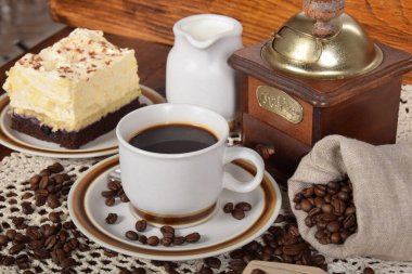 Kahve makinesinin yanında kahve fincanının içinde kahve çekirdeği ve kek.