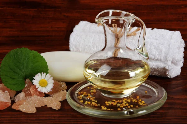 a glass jug with body oil standing on a glass plate with pollen from flowers