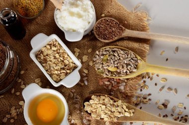 Çiğ tavuk yumurta sarısı, ahşap kaşıklar ve Himalaya tuzu, keten tohumu, ayçiçeği tohumu ve yulaf ezmesi dolu çeşitli kaplar.