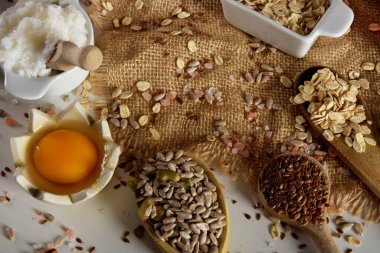 Çiğ tavuk yumurta sarısı, ahşap kaşıklar ve Himalaya tuzu, keten tohumu, ayçiçeği tohumu ve yulaf ezmesi dolu çeşitli kaplar.