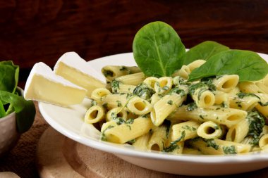 Beyaz tabakta ıspanak soslu makarna yanında taze ıspanak yaprakları ve ahşap mutfak tahtasındaki mavi peynir.