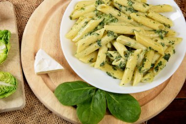 Soslu makarna, ıspanak ve peynirle ahşap mutfak tahtasındaki beyaz kasede.