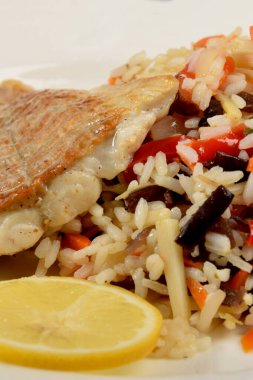 Sebzeli renkli pirinç ve beyaz tabakta kızarmış balık.