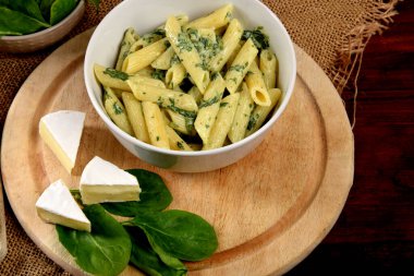 Kremalı ıspanak soslu makarna taze ıspanak yaprakları ve ahşap mutfak tahtasının üstünde mavi peynir.