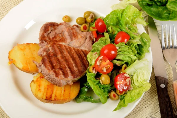 白皿の上にトマトとオリーブのレタスの横に焼きジャガイモと焼き肉が2つ — ストック写真