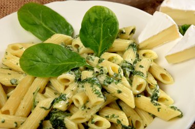 Beyaz tabakta ıspanak soslu makarna yanında taze ıspanak yaprakları ve ahşap mutfak tahtasındaki mavi peynir.