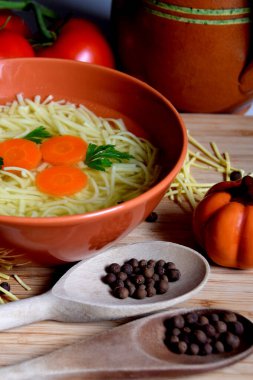 Domateslerin, baharatların ve mutfak malzemelerinin yanında bir kasede leziz tavuk suyu çorbası.