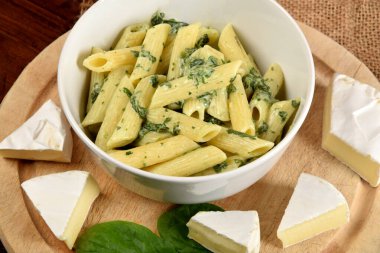 Soslu makarna, ıspanak ve peynirle ahşap mutfak tahtasındaki beyaz kasede.