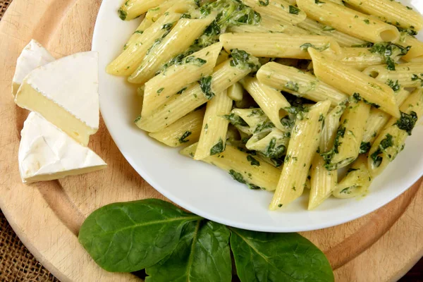 penne in a sauce with spinach and cheese in a white bowl on a wooden kitchen board